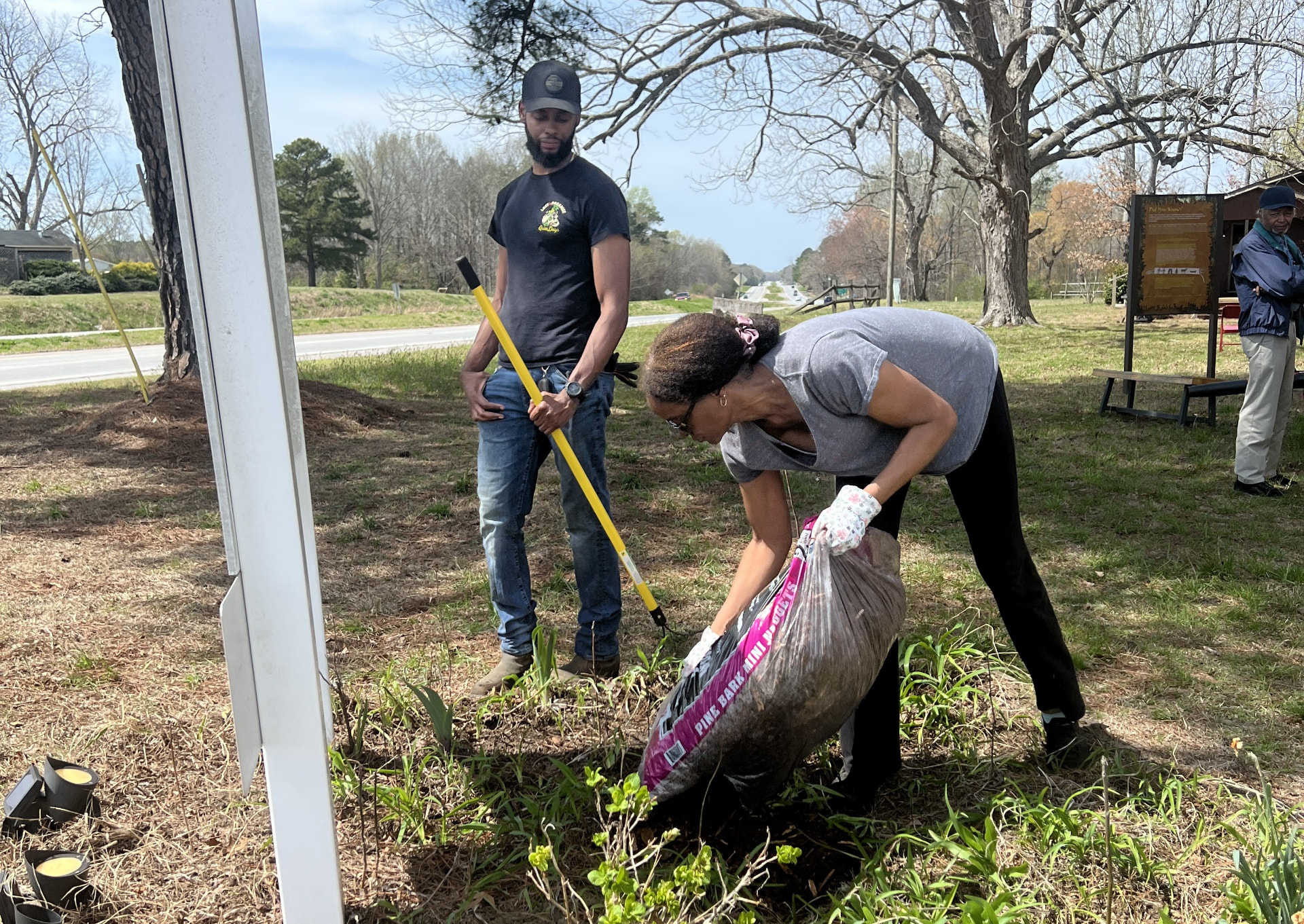 Volunteers spreading pine bark mulch in a garden bed