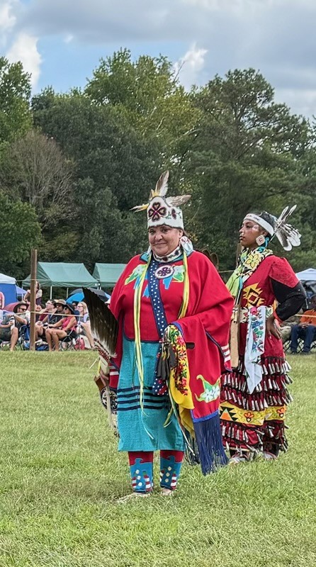 Two women in bright traditional dance regalia standing on the field at the powwow