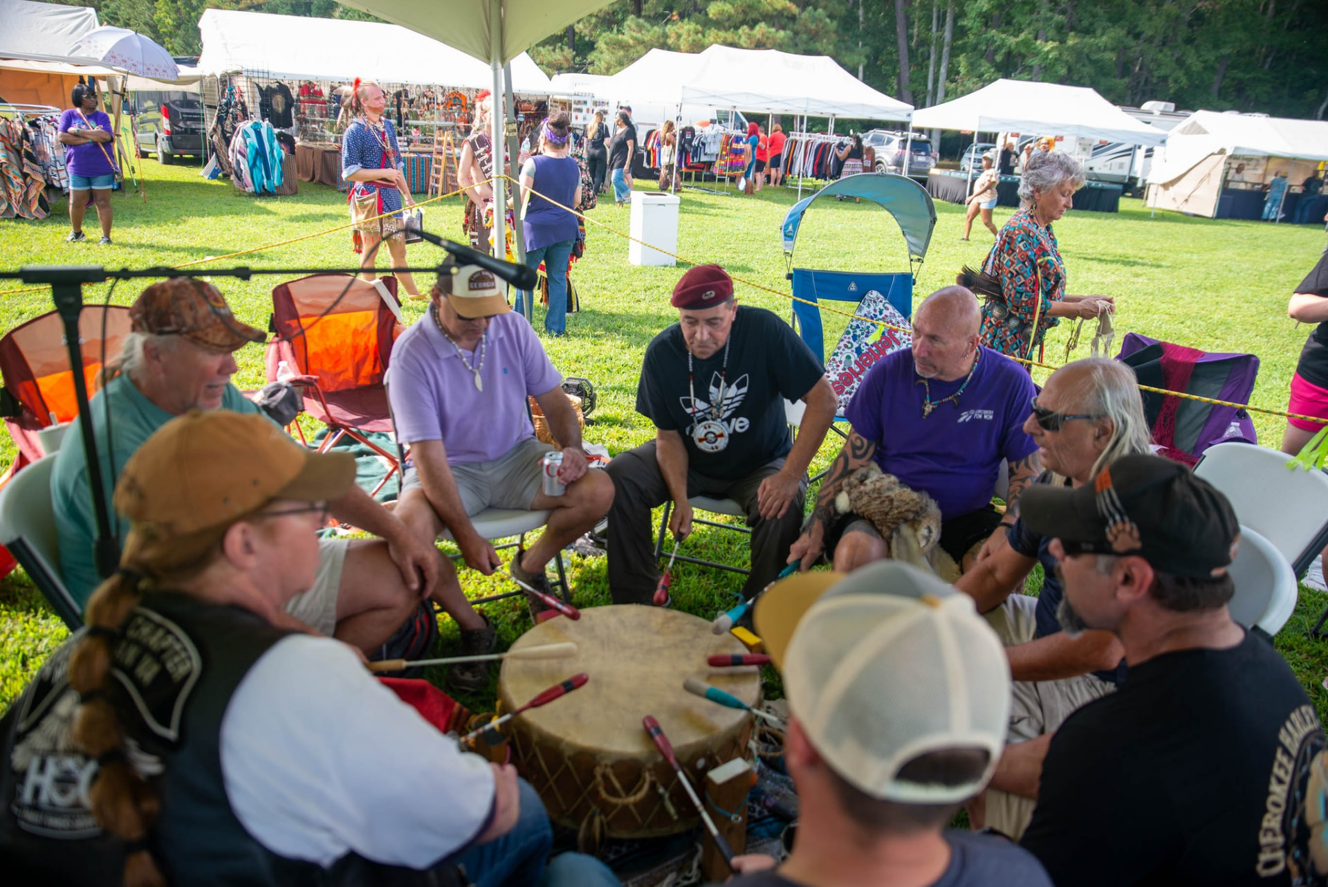 A drum group seated in a circle around a large drum at an outdoor powwow