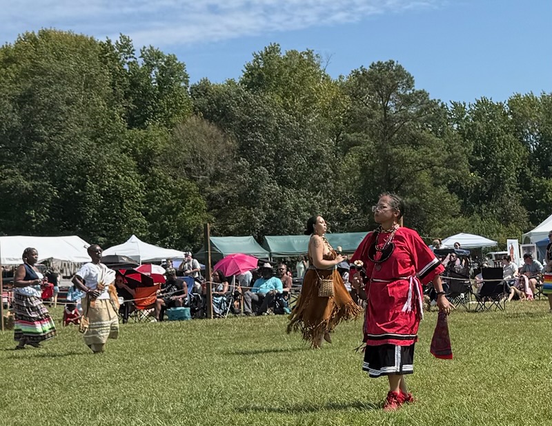 Dancers in traditional regalia on the field with the audience seated behind the rope line