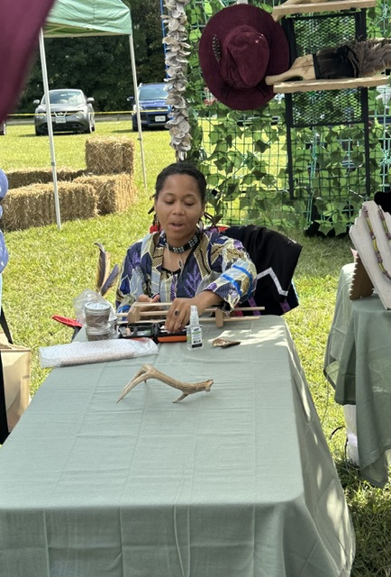 A tribal member working on a craft at the table inside the vendor tent