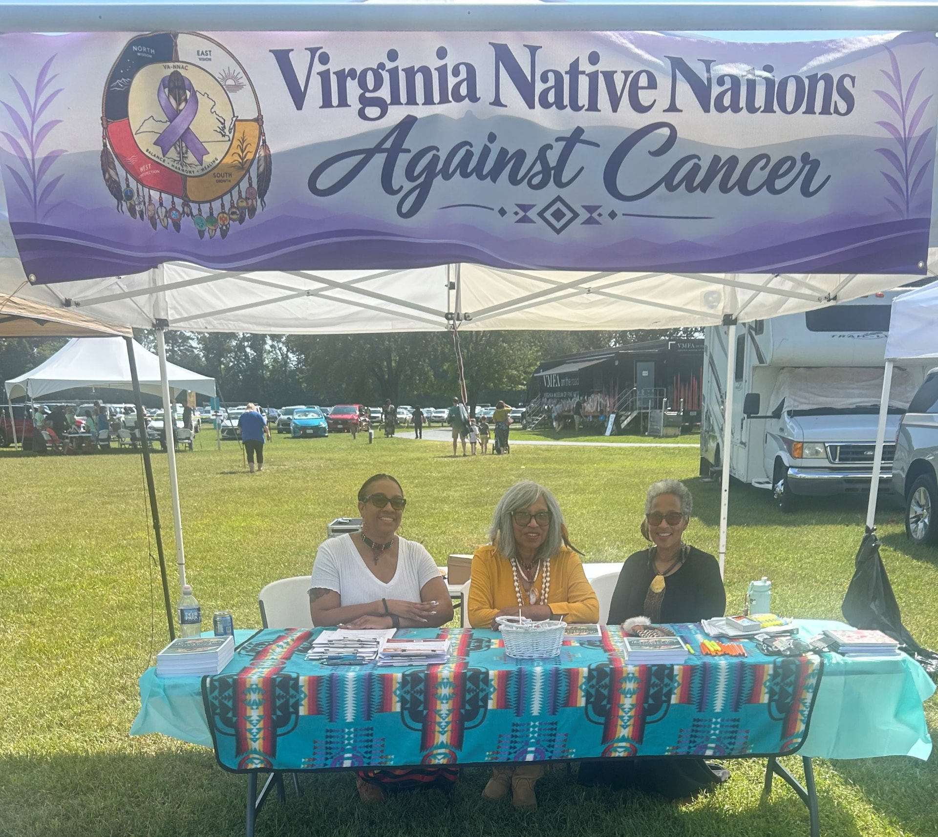 Three women seated at the Virginia Native Nations Against Cancer booth at the 2026 Powwow