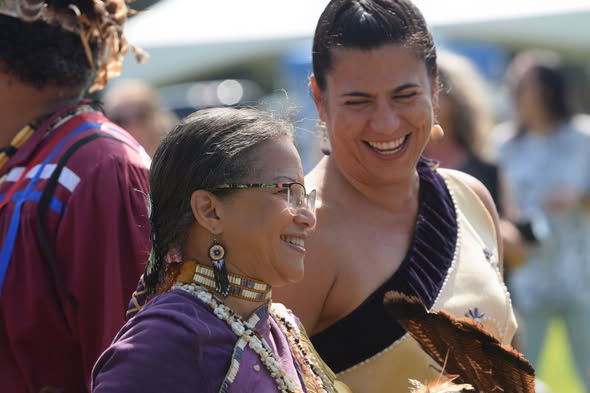 Two Nottoway women in regalia sharing a laugh at a tribal gathering