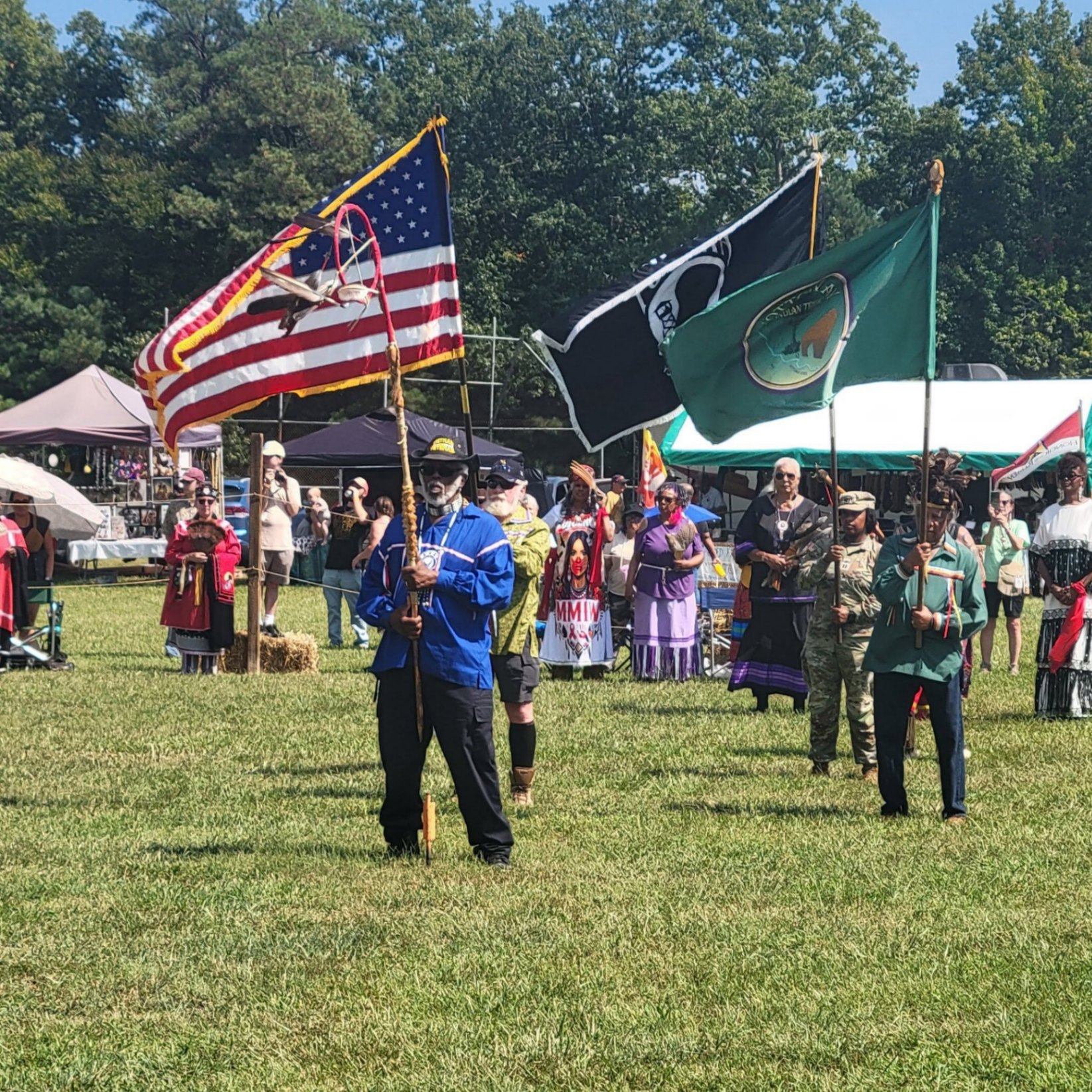 The color guard carrying the American flag, a black flag, and the tribe's green flag at the 2026 powwow
