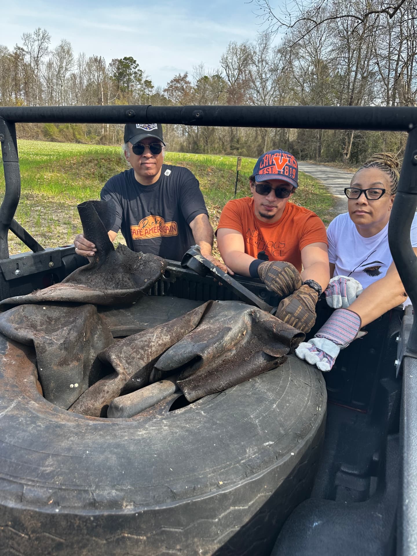 Three volunteers with a large tire and debris loaded in the back of a utility vehicle